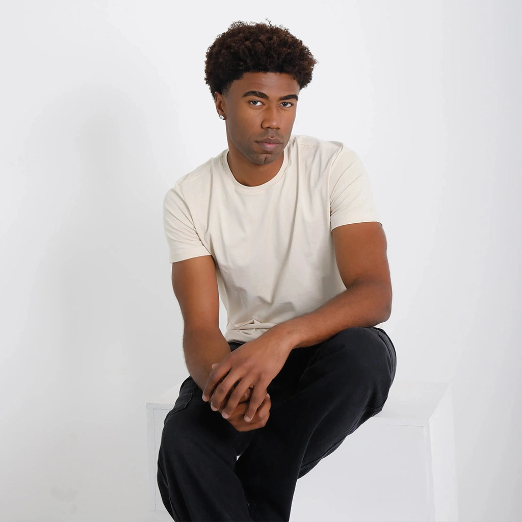 Camiseta Basica Algodao Egipcio cru, cena sentada; superfície lisa, caimento confortável e tom off-white.