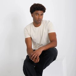 Camiseta Basica Algodao Egipcio cru, cena sentada; superfície lisa, caimento confortável e tom off-white.