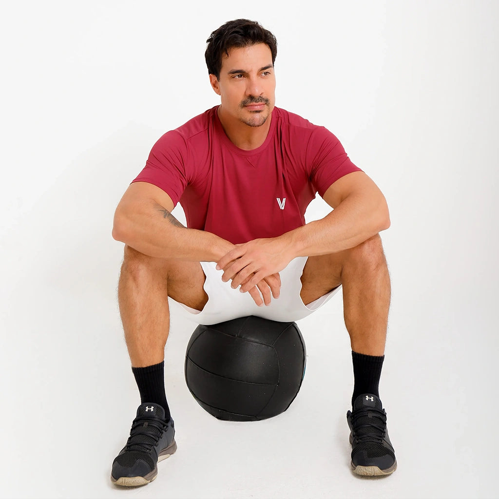 Camisetas Poliamida Esportiva bordô em uso casual esportivo, modelo sentado com short claro.