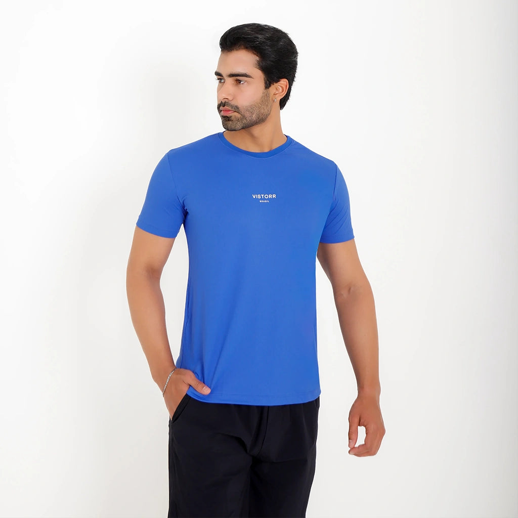 Modelo usando Camisetas Poliamida UV30 azul em fundo branco, com uma mão no bolso.