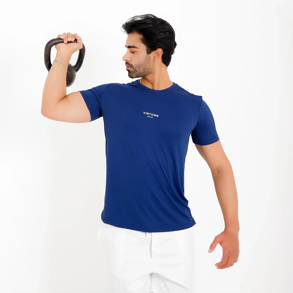 Camisetas Poliamida UV30 azul-marinho, pose ativa com kettlebell; logo central pequeno, caimento leve.