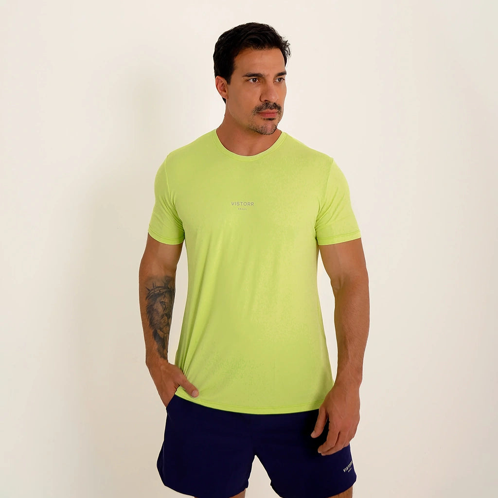 Modelo em ângulo usando Camisetas Poliamida UV30 verde claro em fundo branco, com mão no bolso.