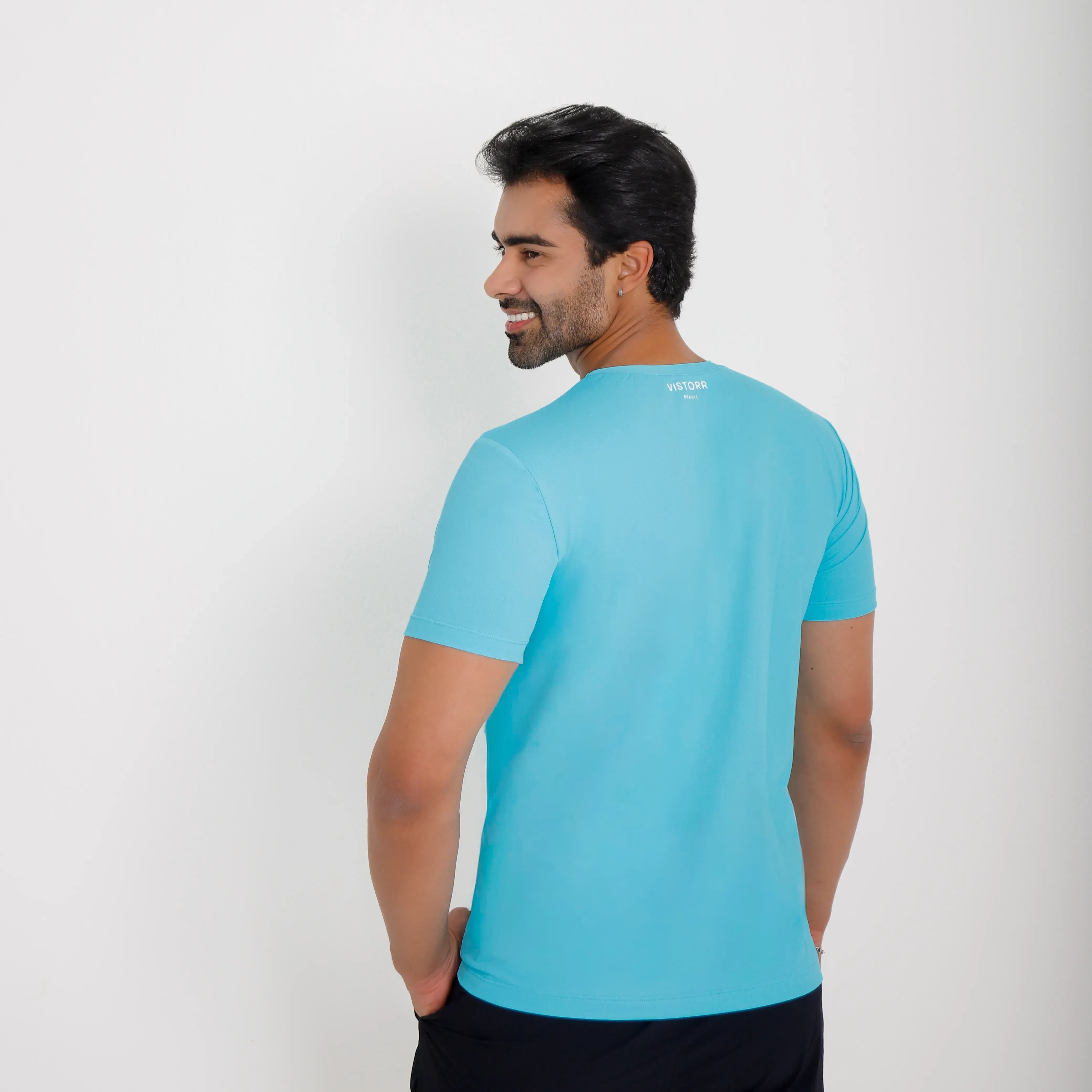 camiseta poliamida vistorr v azul claro costas - modelo em posicao corporal de costas, com rosto virado sorrindo